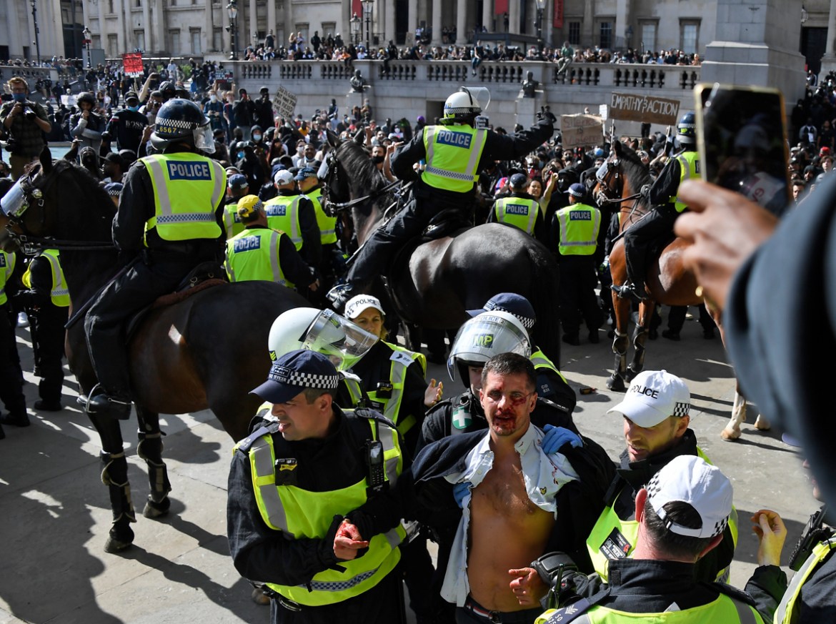 A wounded member of a far-right group is escorted by British police officers in riot gear, during scuffles as they try to contain a protest at Trafalgar Square in central London, Saturday, June 13, 20