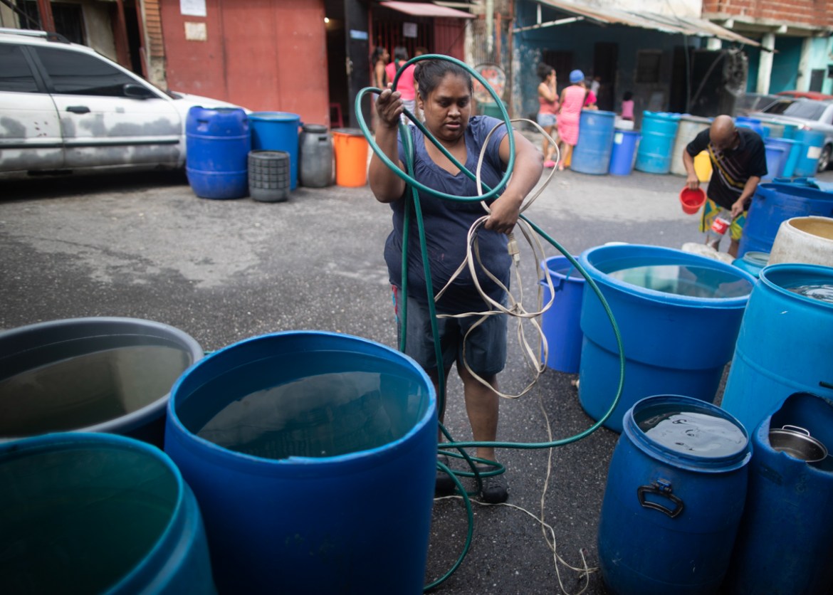 A woman untangles an electrical cord and a hose in order to pump from a large container water provided by a government water truck, in the Petare slum of Caracas, Venezuela, Wednesday, June 10, 2020.