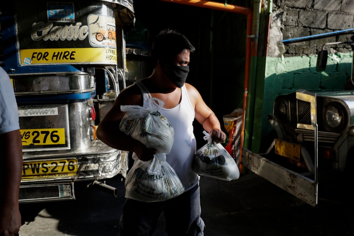 A jeepney driver carries relief goods donated by a Catholic church at the Tandang Sora terminal which have been home for them since a lockdown started three months ago, on Wednesday, June 17, 2020 in
