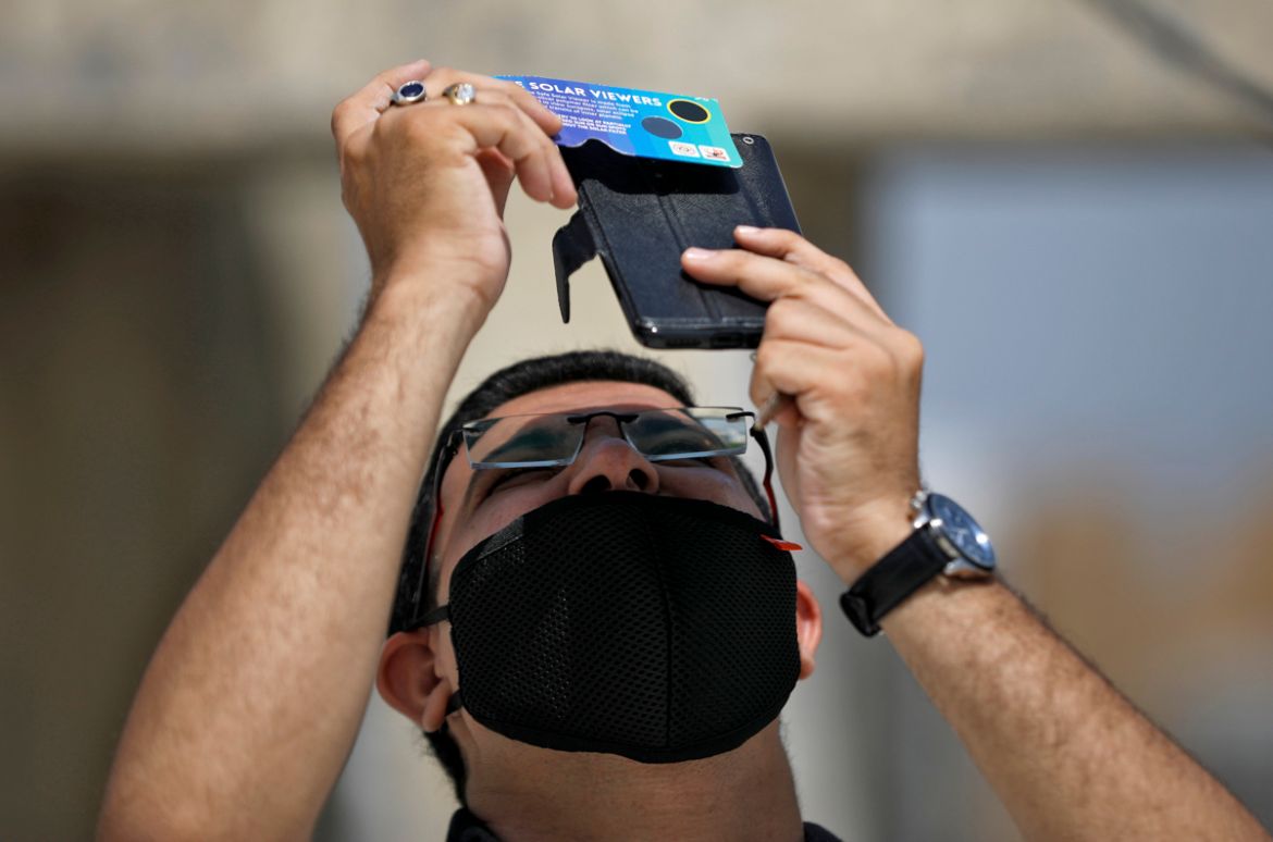 A man, wearing a protective face mask against the coronavirus disease (COVID-19), uses his mobile phone and solar viewers to take photographs of a partial solar eclipse at Gandhinagar, India, June 21,