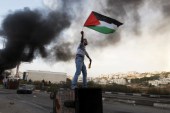 A Palestinian man waves the national flag during a protest against Israel's operations in Gaza Strip, near the West Bank city of Ramallah, on Nov 18, 2012 [AP Photo/Majdi Mohammed]