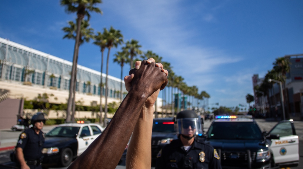 A black man and a white woman hold their hands up in a front of police officers in downtown Long Beach on May 31, 2020 during a protest against the death of George Floyd, an unarmed black man who died