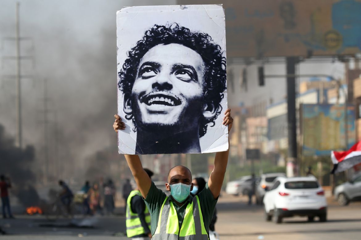 A mask-clad man holds a picture of a Abdulsalam Kisha, a Sudanese protester who was killed in a raid on an anti-government sit-in in 2019, during a protest in the Riyadh district in the east of the ca