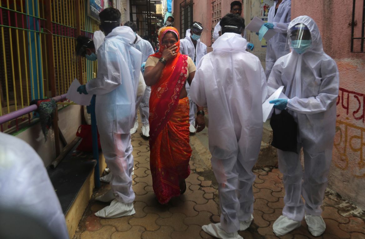 A woman covers her face as she walks past health workers arriving to administer a free medical checkup in a slum in Mumbai, India, Sunday, June 28, 2020. India is the fourth hardest-hit country by the