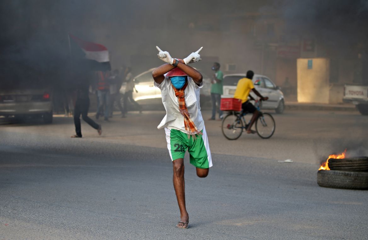 A Sudanese protester clad in mask and latex gloves runs during a demonstration marking the first anniversary of a raid on an anti-government sit-in, in the Riyadh district in the east of the capital K