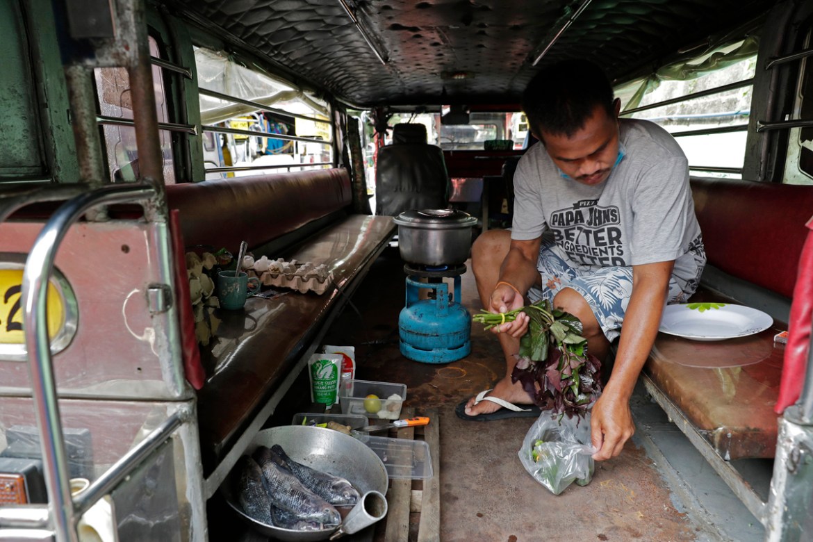 Driver Michael Navarra cooks fish and vegetables on their portable stove inside a jeepney at the Tandang Sora terminal which have been home for them since the lockdown started three months ago, on Wed