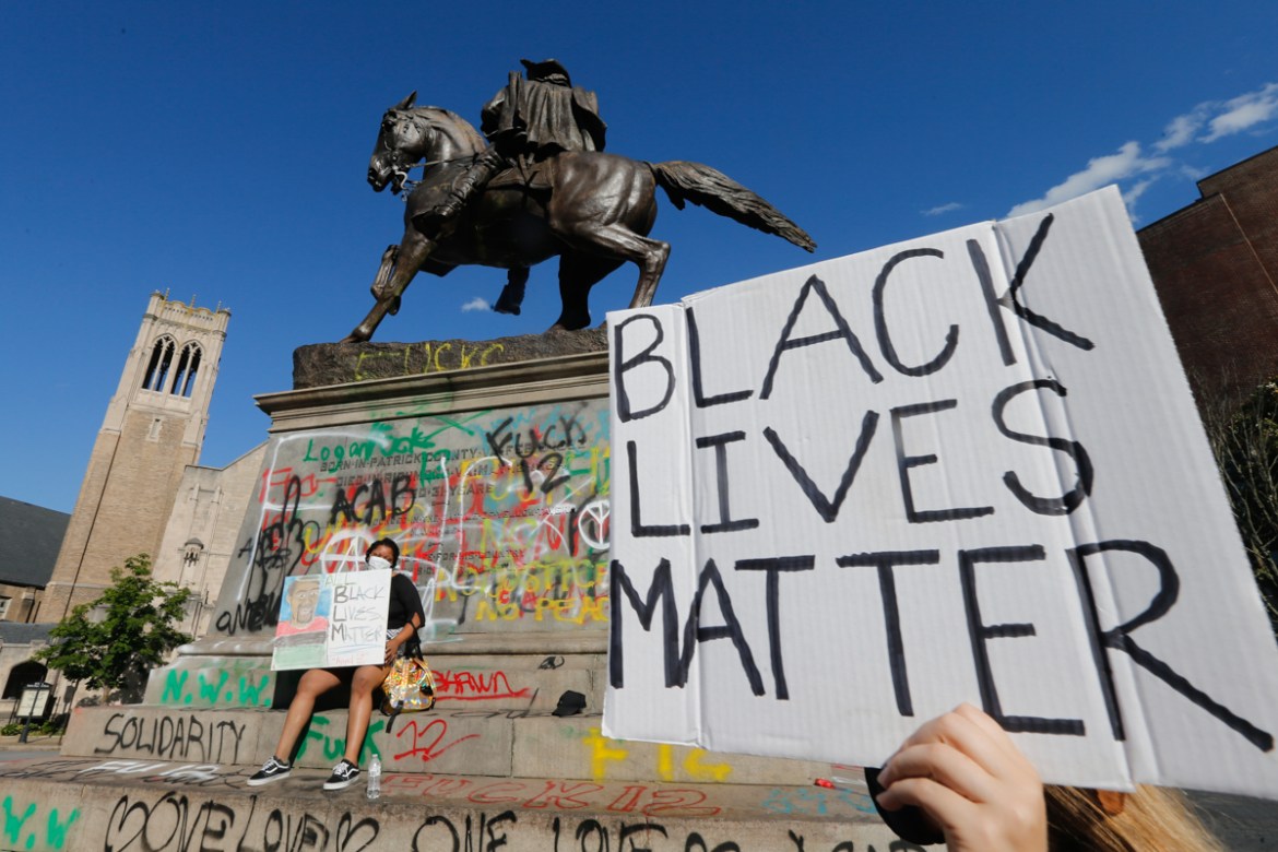 Demonstrators hold signs near the graffiti covered statue of Confederate General J.E.B. Stuart after two previous nights of unrest due to the death of George Lloyd Sunday May 31, 2020, in Richmond, Va