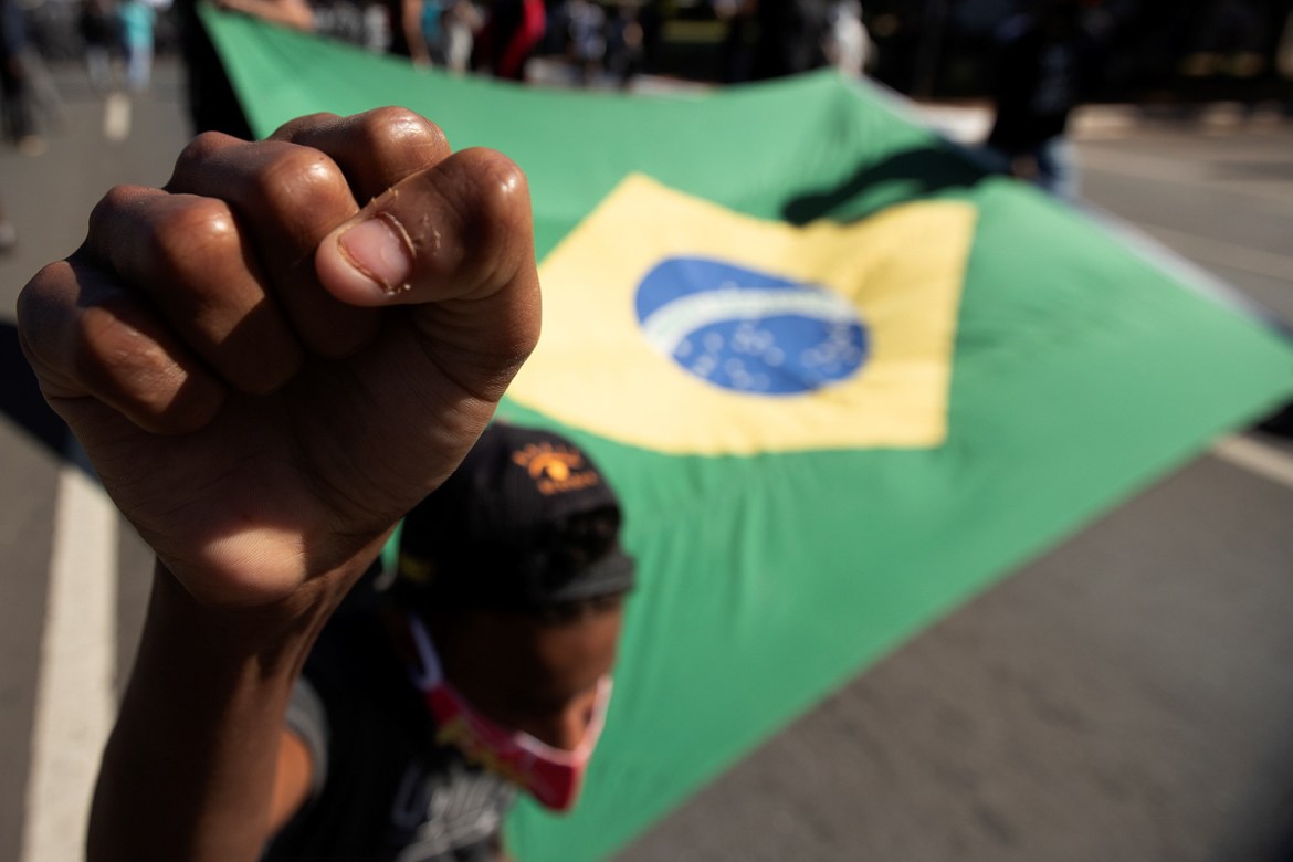 epa08471412 A participant raises a fist next to a Brazilian flag during the protest against the President of Brazil Jair Bolsonaro, defending democracy, and condemning racism and fascism, in Brasilia