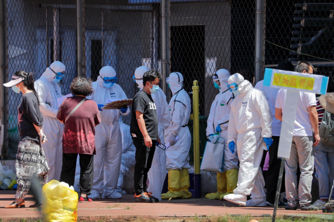 Workers in protective suits check people''s names on the list who were either living surrounding the Xinfadi wholesale market or have visited to the market to get a nucleic acid test at a stadium in Be