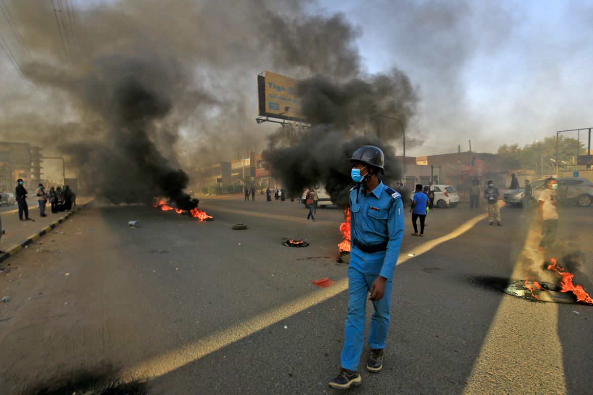 A mask-clad policeman walks near tires set aflame by Sudanese protesters marking the first anniversary of a raid on an anti-government sit-in, in the Riyadh district in the east of the capital Khartou
