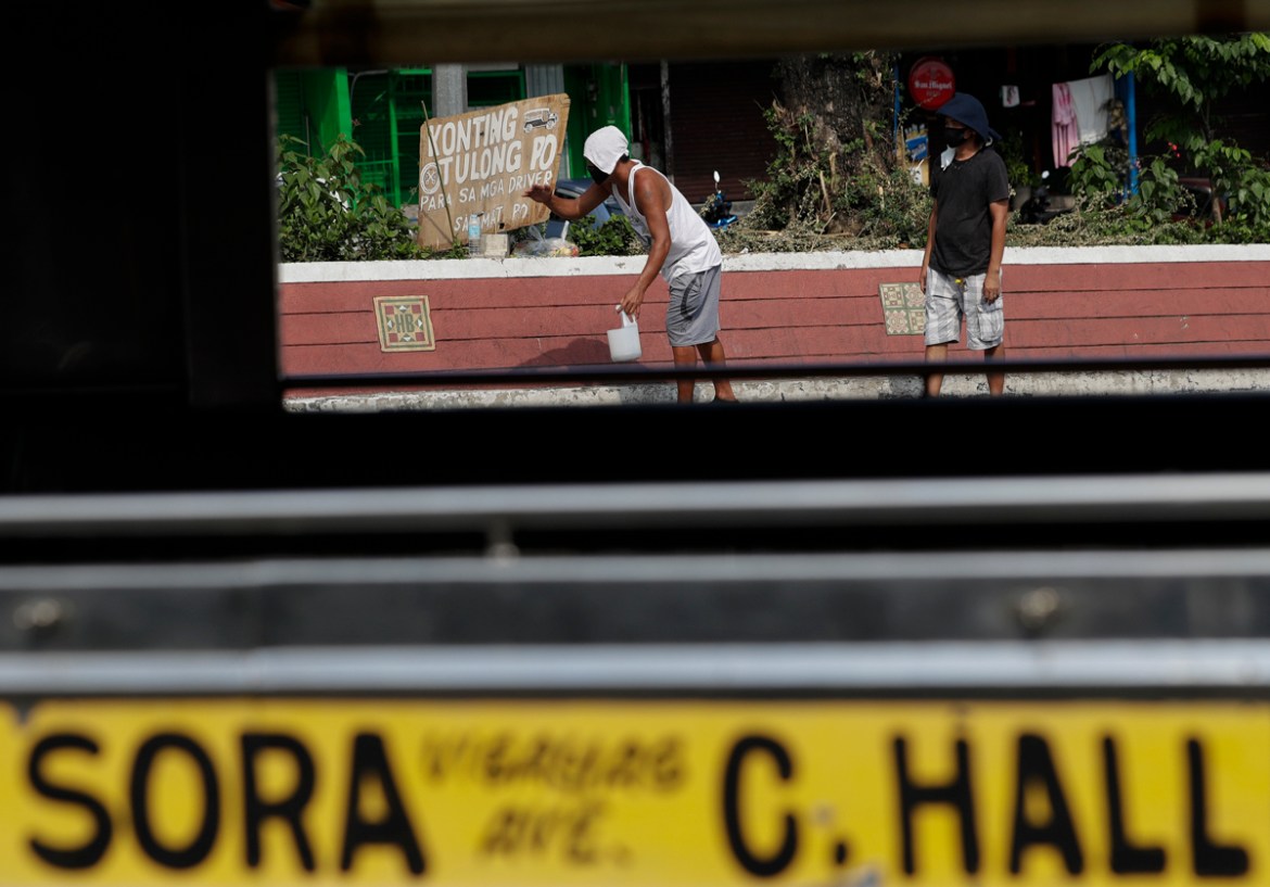 Jeepney drivers beg for money beside a sign that says "a little help please for the drivers, thank you" in front of the Tandang Sora terminal which have been home for them since a lockdown started thr