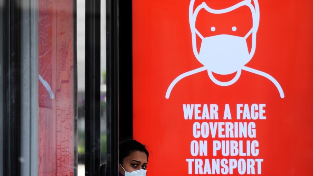 A woman wearing a protective face mask is seen at a bus stop with a p