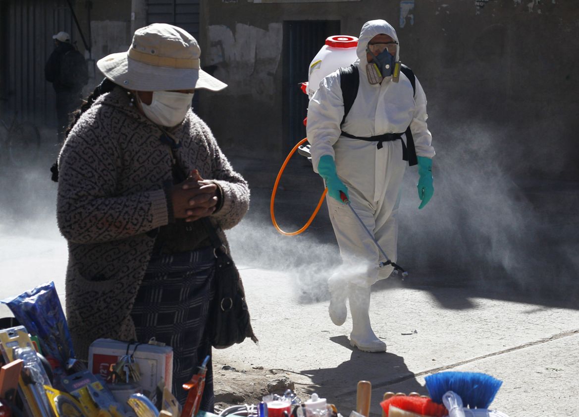 A municipal worker sprays disinfectant past a street vendor at a market in Puno, Peru, near the border with Bolivia, on June 10, 2020. - The inhabitants of the Andean heights of Bolivia and Peru have