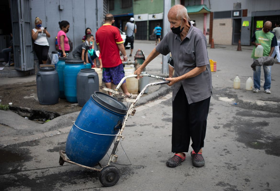 A man, wearing a protective face mask, pushes a dolly holding a container filled with water he collected from a street faucet, in Caracas, Venezuela, Saturday, June 20, 2020. Water service in Venezuel