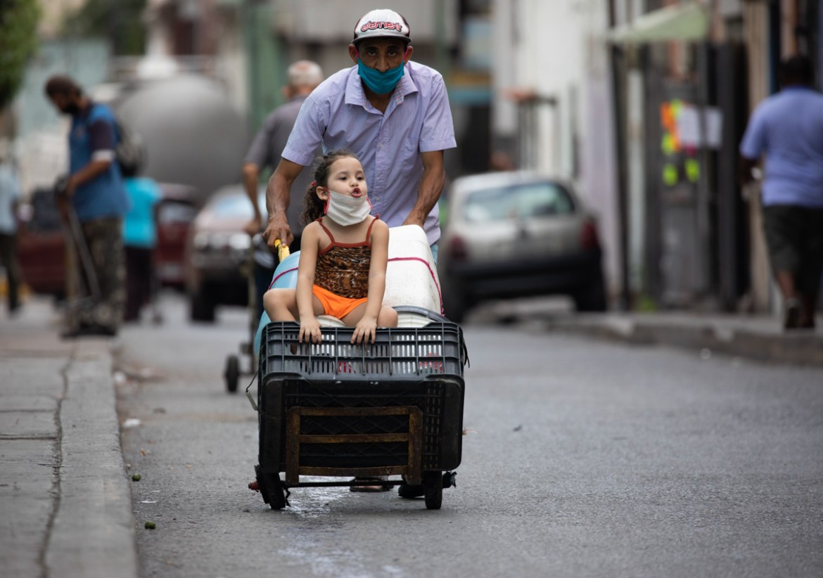 A man, wearing a protective face mask, pushes a dolly filled with empty containers, as he and a child go in search of water in Caracas, Venezuela, Saturday, June 20, 2020, during a relaxation of restr