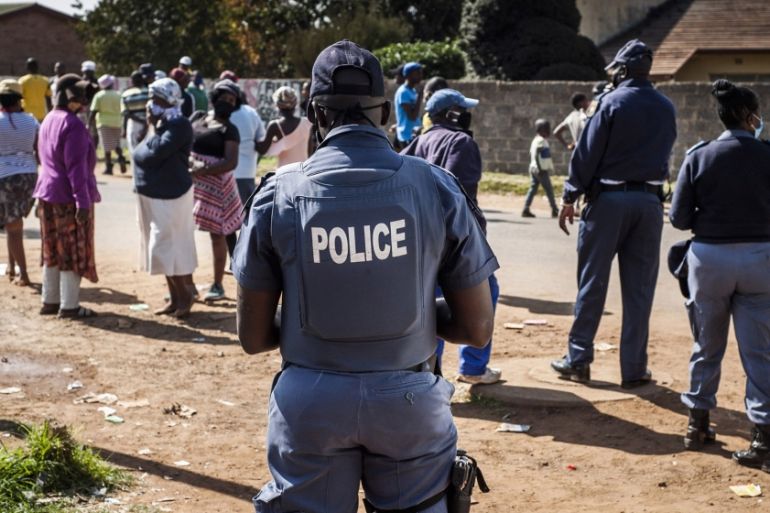 A police officer patrols as residents queue to receive parcels of food aid at a distribution point at the Zenzele Counselling Project in Finetown, south of Johannesburg, on Thursday, May 7, 2020. Almo