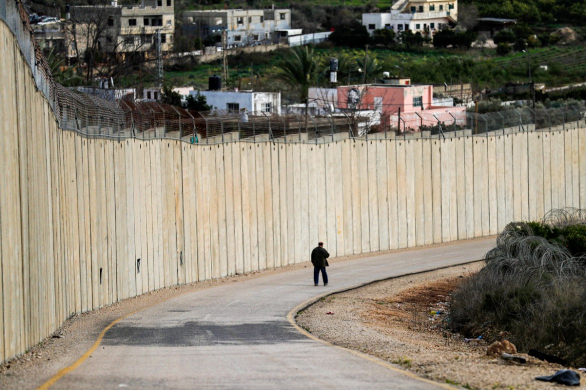 A man walks along a road by Israel''s controversial separation barrier between the occupied West Bank village of Nazlat Issa (L) and the Arab-Israeli town of Baqa al-Gharbiya (R) in northern Israel on