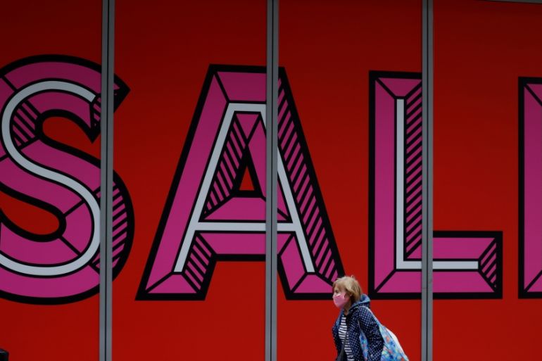 A woman wearing a protective face covering walks past a sale sign in a shop window following the outbreak of the coronavirus disease (COVID-19), in Manchester, Britain