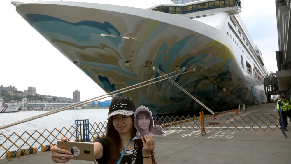 A woman takes a selfie in front of the Explorer Dream cruise ship, in Keelung