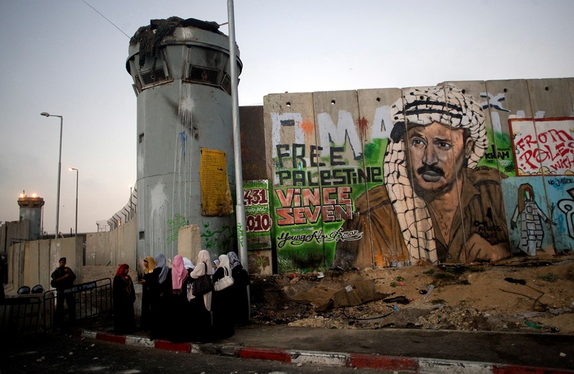 File - In this Friday, Aug. 13, 2010 file photo, Palestinian women wait near a section of Israel''s separation barrier covered in graffiti, one depicting the late Palestinian leader Yasser Arafat, at t