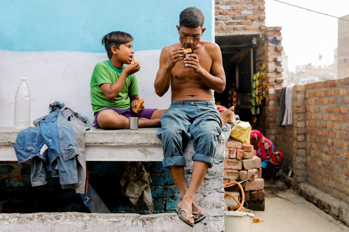 Mansoor Khan, 44, who works as a waste collector, eats breakfast with his son Latif Khan, 11, outside their house which is next to a landfill site, during the coronavirus disease (COVID-19) outbreak,