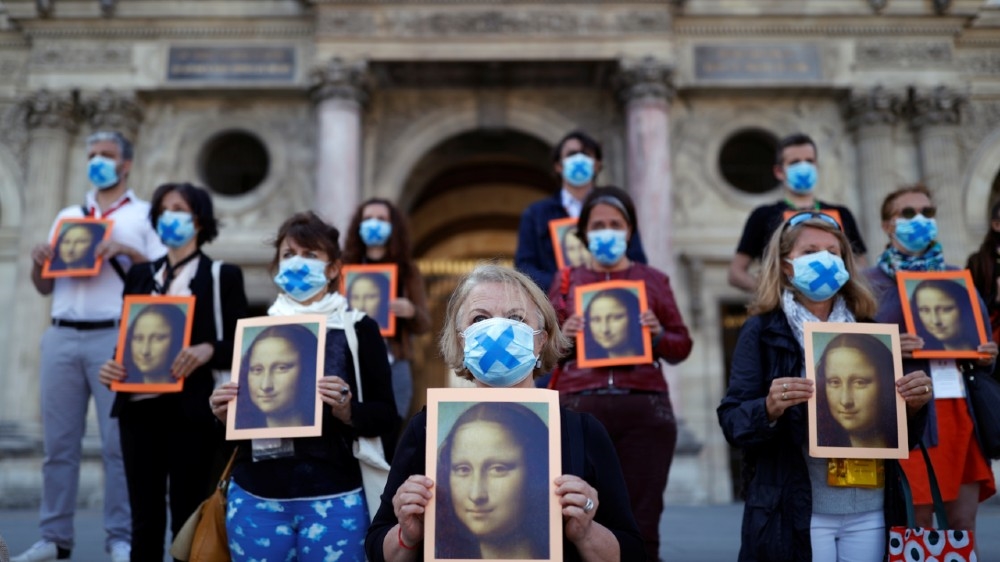 Paris tour guides hold posters depicting Mona Lisa painting by artist Leonardo da Vinci during an action at Le Louvre museum courtyard to warn on their working conditions