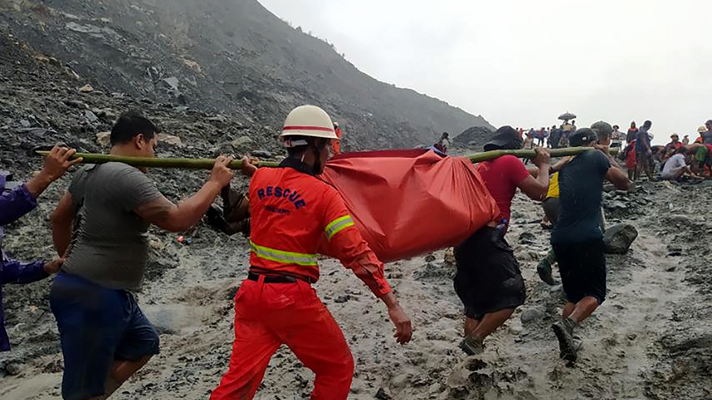 epa08522227 A handout photo made available by the Myanmar Fire Services Department shows rescue workers carrying the body of a victim after a landslide accident at a jade mining site in Hpakant, Kachi