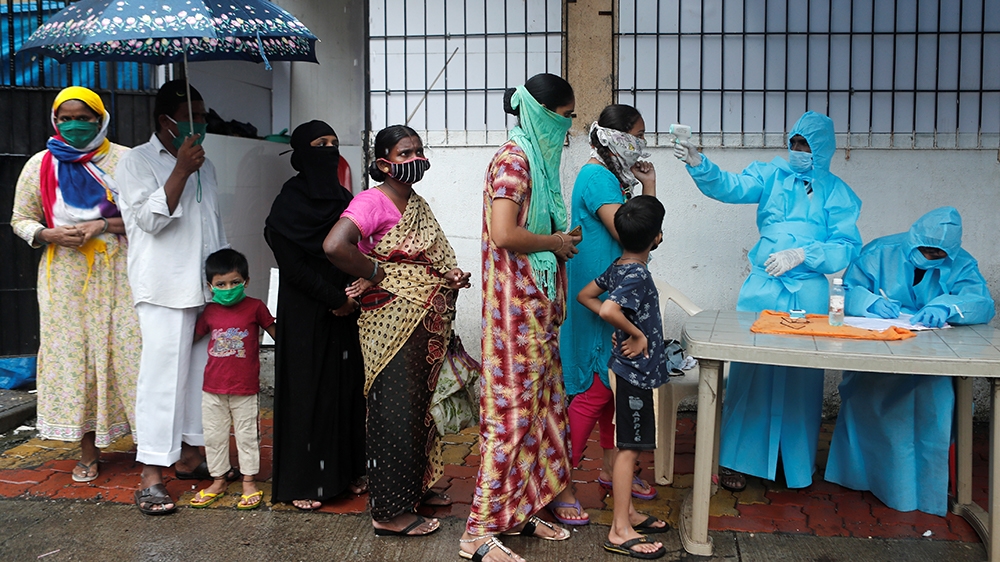People stand in a queue as a healthcare worker checks the temperature of a resident using an electronic thermometer during a medical campaign for the coronavirus disease (COVID-19) in Mumbai, India, J