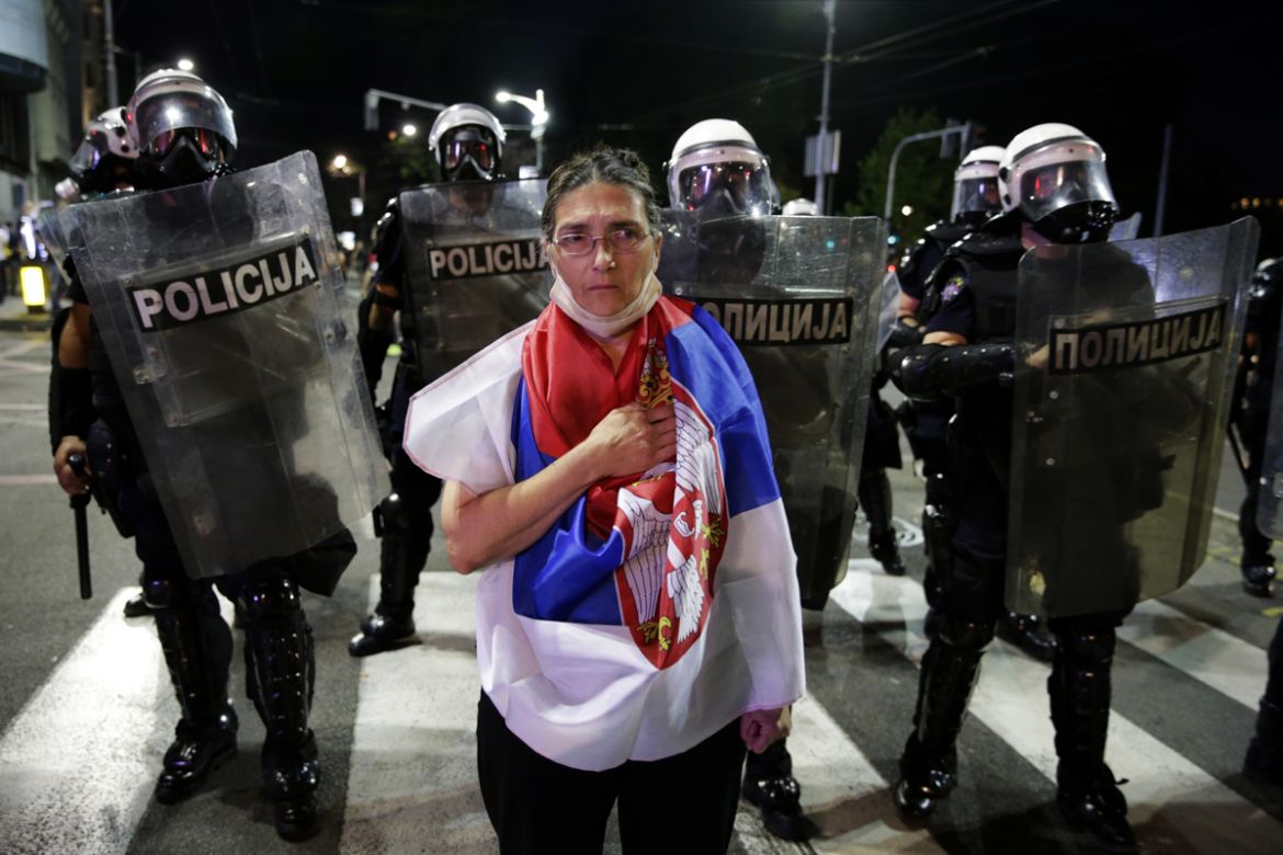 epa08535587 A protestor wearing a wrapped in Serbian flag stands in front of a police line in front of the Serbian Parliament in Belgrade, Serbia, 08 July 2020. Thousands have gathered in front of the