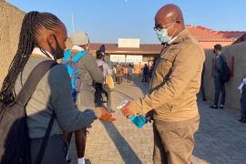 A staff member sanitizes the hands of students as schools begin to reopen after the coronavirus disease (COVID-19) lockdown in Soweto