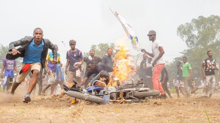 Demonstrators stand next to a burning motorcycle during a protest where demonstrators and police officers clashed in Kinshasa on July 9, 2020 in demonstrations organized