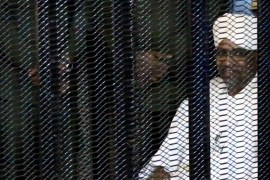 Sudan''s former president Omar Hassan al-Bashir sits guarded inside a cage at the courthouse where he is facing corruption charges, in Khartoum