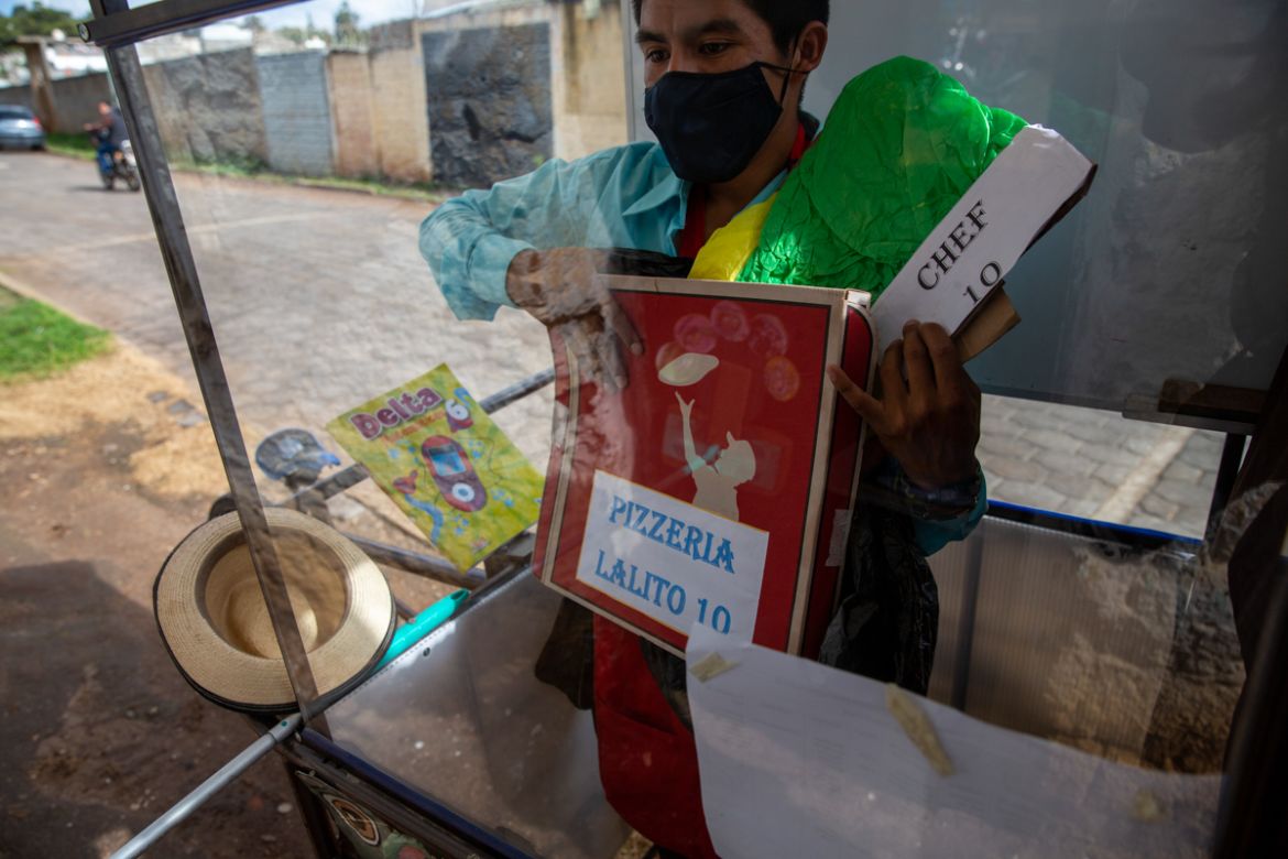 Standing behind the plexiglass window of his mobile classroom, Gerardo Ixcoy holds a pizza box as part of a lesson on fractions, in Santa Cruz del Quiche, Guatemala, Wednesday, July 15, 2020. "I tried