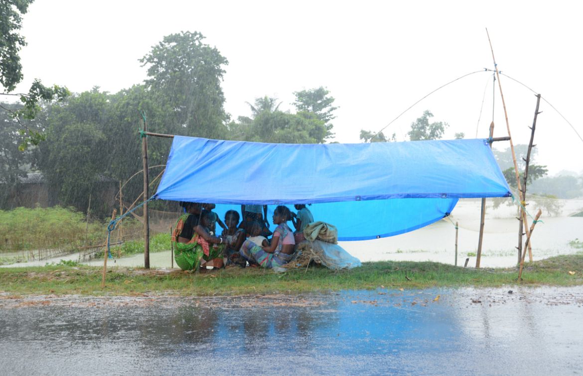 epa08554576 Flood affected villagers sit under a temporary shelter during rainfall in a flood affected area in Morigaon district of Assam, India, 19 July 2020. According to news reports, Assam state c