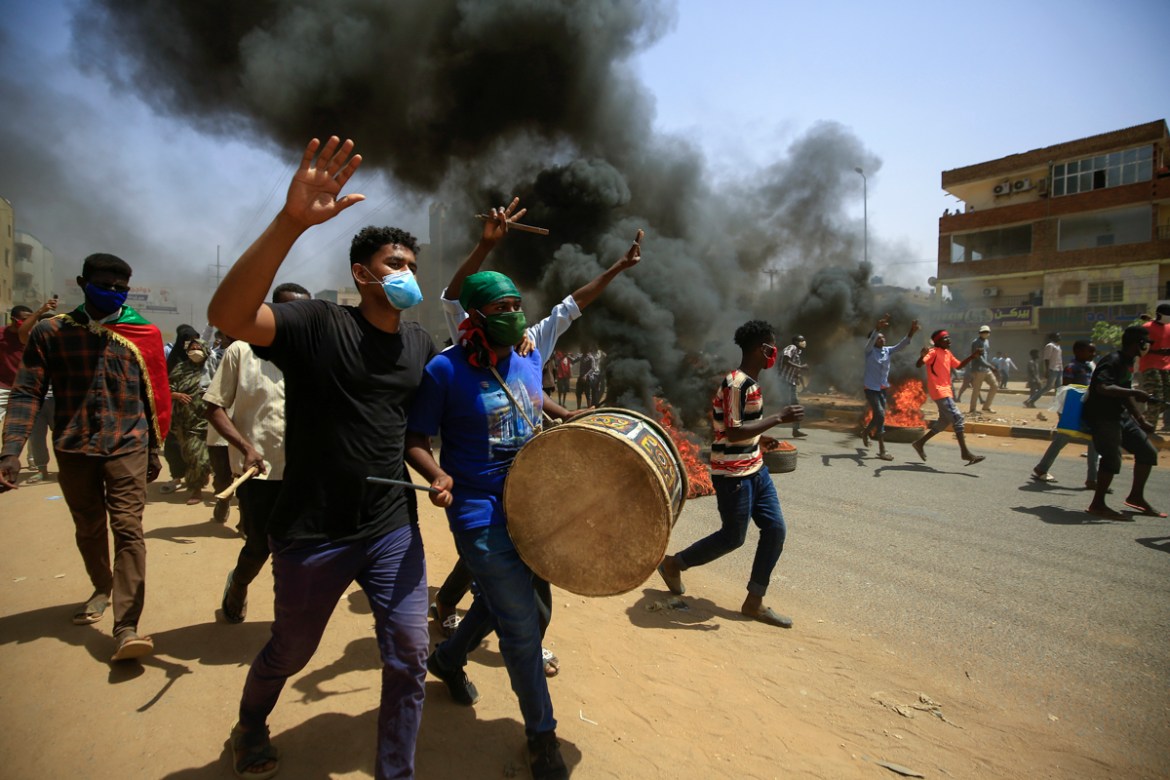 Sudanese demonstrators carrying a drum gesture as smoke billows from burning tyres during a protest on Sixty street in the east of the capital Khartoum, on June 30, 2020. - Tens of thousands of Sudane