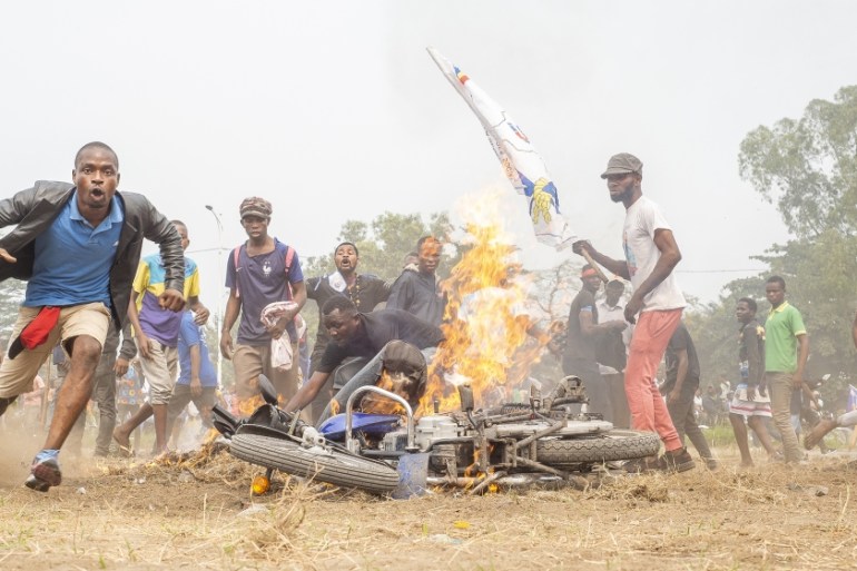 Demonstrators stand next to a burning motorcycle during a protest where demonstrators and police officers clashed in Kinshasa on July 9, 2020 in demonstrations organized against the presidential party