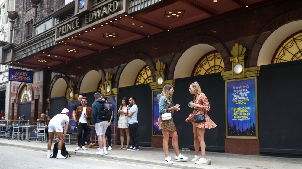Customers of a bar stand drinking outside the closed Prince Edward theater in London, U.K., on Saturday, July 4, 2020. Restaurants, hotels, cinemas and hairdressers will also be allowed to open their 