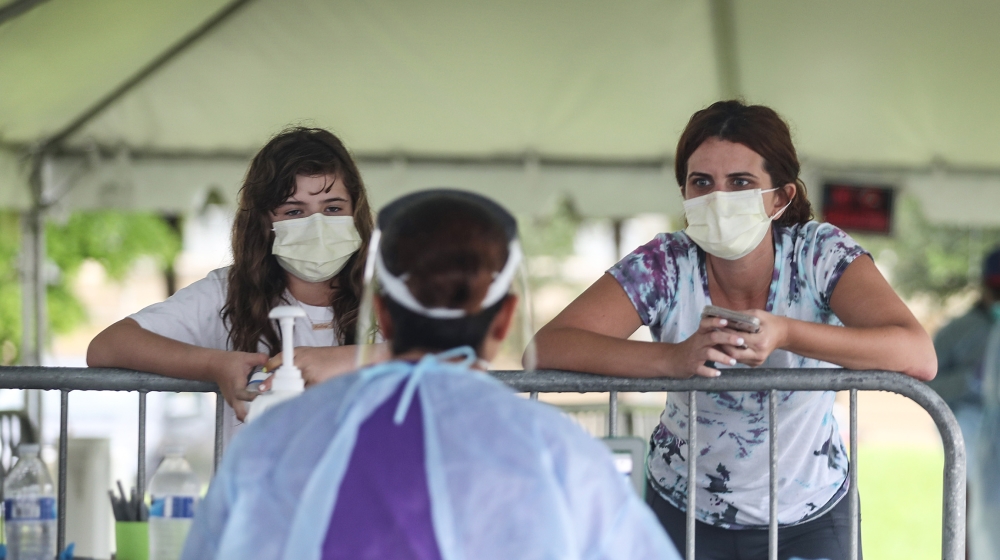 Health care workers take information from Ashley Perez and her daughter Hailey Garcia before they are tested for COVID-19 in a medical tent at a testing site locate at the Miami Lakes Youth Center on 
