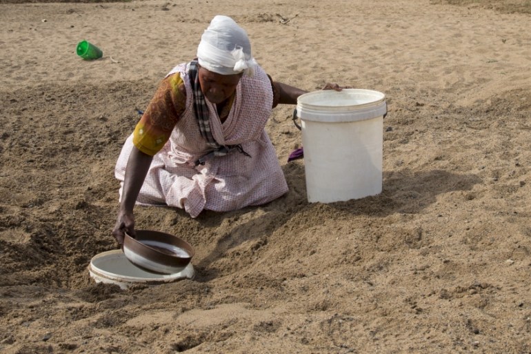 A woman gets water from a well dug in the Black Imfolozi River bed, which is dry due to drought, near Ulundi