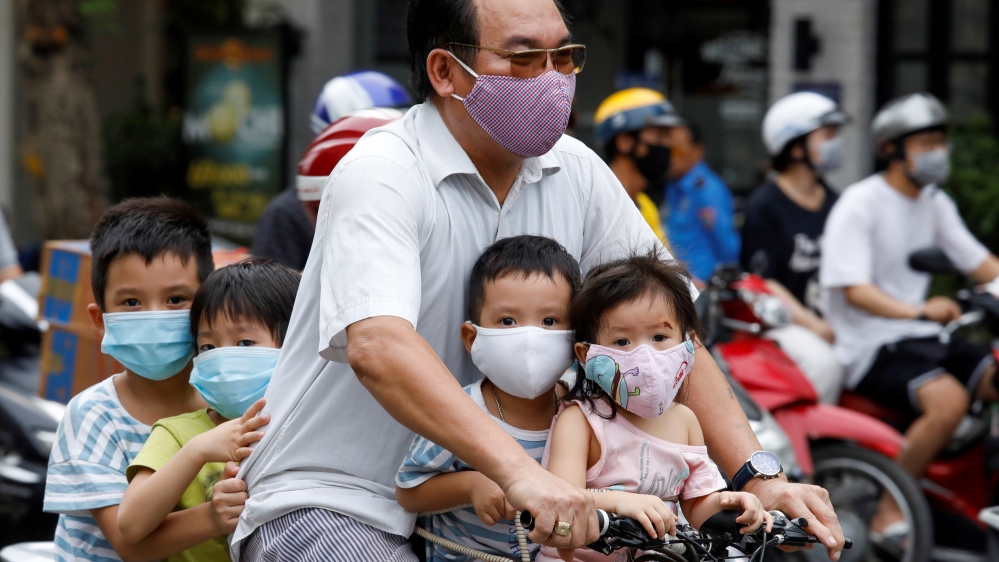A man and his children, all wearing protective masks, ride a bicycle on a street in Hanoi