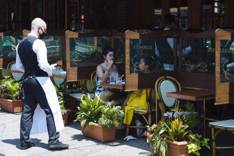 A server wearing a protective mask assists customers dining outside at a restaurant in the Greenwich Village neighborhood of New York, U.S., on Monday, July 6, 2020. New York City delayed the return o