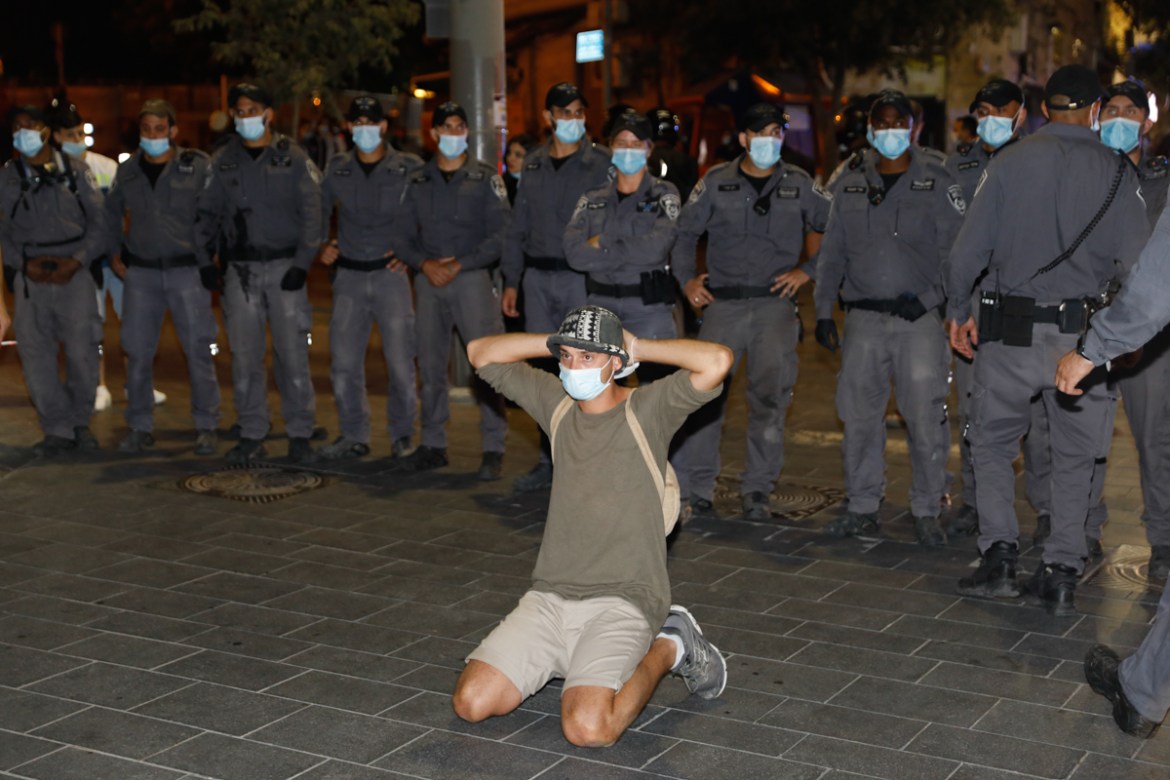 A protester kneels in front of a row of police during a demonstration against the Israeli prime minister in Jerusalem, on July 14, 2020. - Israeli Prime Minister Benjamin Netanyahu, 70, was indicted