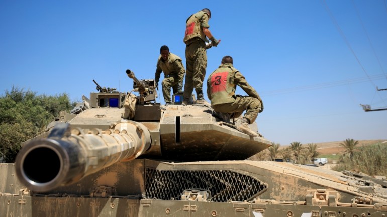 Israeli soldiers stand atop a tank near the border between Israel and the Gaza Strip