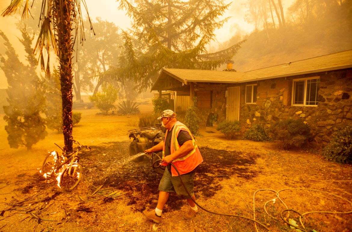 A resident hoses down a burning bicycle and tree as flames from the Hennessey approach a property in the Spanish Flat area of Napa, California on August 18, 2020. - As of the late hours of August 18,