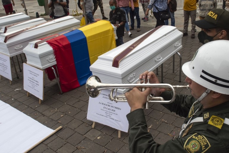 A policeman plays a trumpet next to a set of coffins placed as part of a protests against the violence in Colombia, where several masacres happened over the past days, in Medellin, Colombia on August