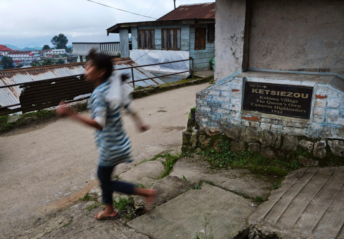A Naga girl runs down a lane with a plaque planted by the British commemorating the Queens Own Cameron Highlanders, an infantry regiment of the British Army, in Kohima village, the site of a bloody WW