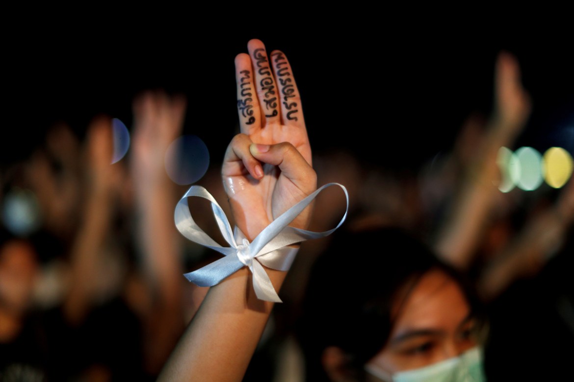 A pro-democracy student wearing a white ribbon does a three-fingered salute with a slogan reading "Freedom, equality and brotherhood" at a rally to demand the government to resign, to dissolve the par