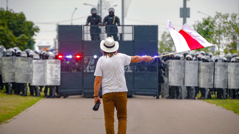 A man waves a historical Belarus flag in front of a riot police blockade during a protest in Minsk, Belarus, Sunday, Aug. 23, 2020. Demonstrators are taking to the streets of the Belarusian capital 