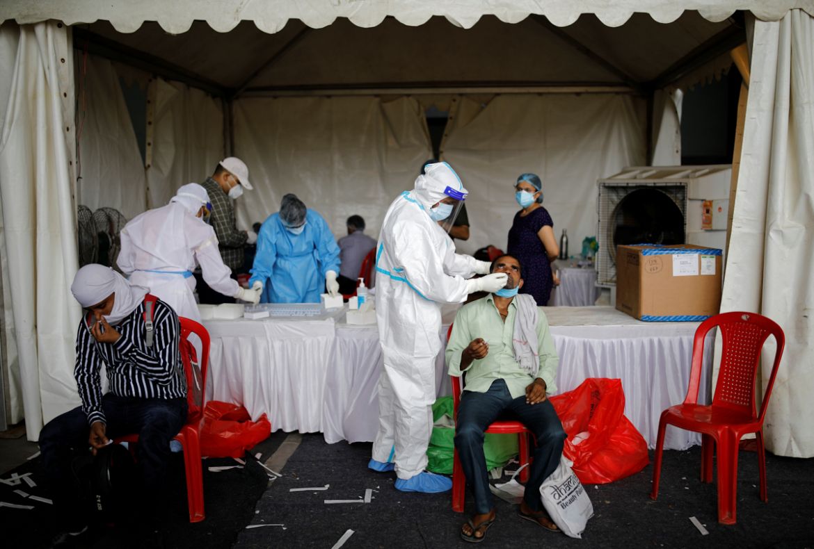 A healthcare worker wearing personal protective equipment (PPE) takes a swab from a migrant worker, who returned to Delhi from his native state, for a rapid antigen test at a bus terminal, amidst the