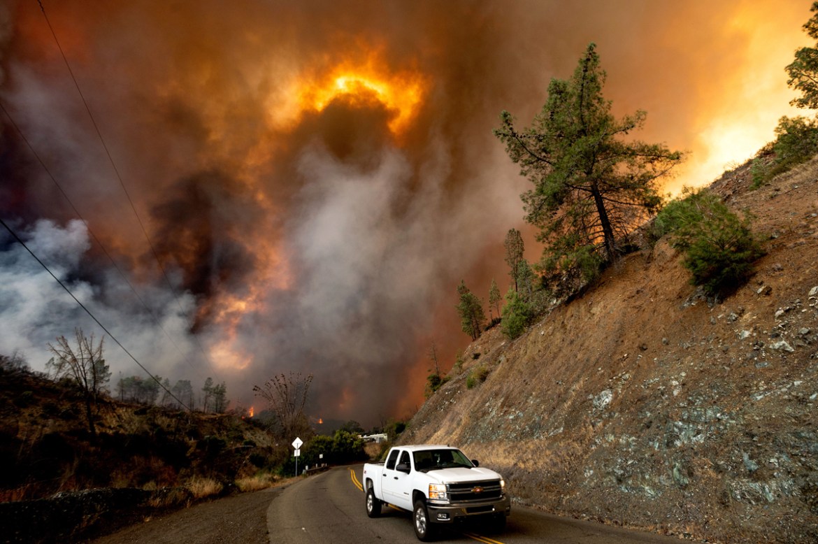 A vehicle drives along Knoxville Road, with flames from the LNU Lightning Complex in the background Tuesday, Aug. 18, 2020, in Napa County, Calif. The blaze went on to destroy multiple homes near Lake